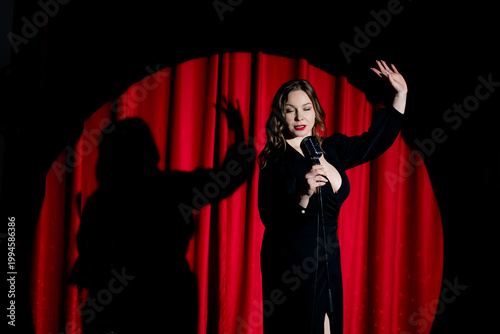 Принти на полотні Female caucasian performer in spotlight on stage with red curtain background