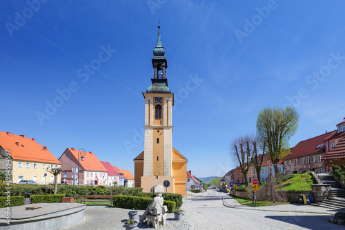 Srebrna Góra, Poland. Clock tower stands in town with colorful buildings under blue sky in early afternoon