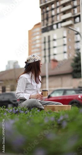 Young Woman Drinking Coffee Sitting On Grass In City Park