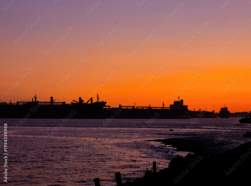 Fototapeta premium A big vessel floating on the water as the sun sets in the background