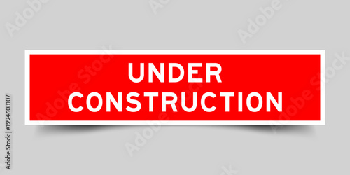 Red color square shape sticker label with word under construction on gray background