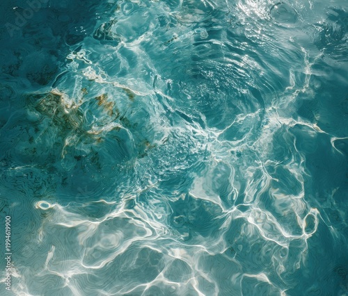 Close up of clear turquoise pool water with bright sunlight reflecting on the surface creating shimmering patterns and light rays with small particles floating beneath the water surface in a vibrant
