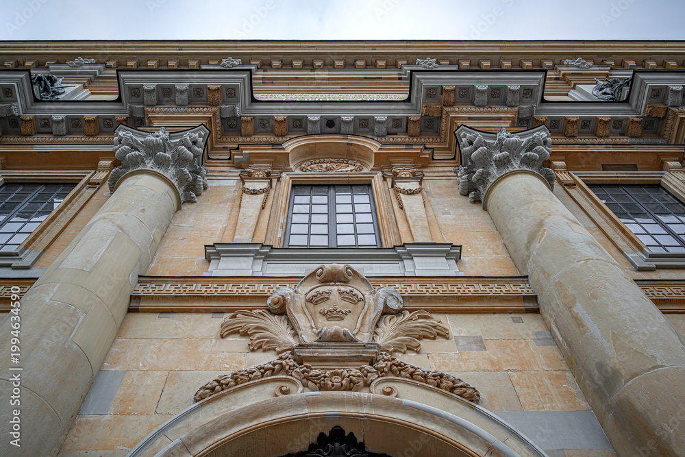 Fototapeta premium Low angle view of the ornate Baroque facade and stone columns of the Royal Palace in Stockholm, featuring the golden Three Crowns heraldic symbol.