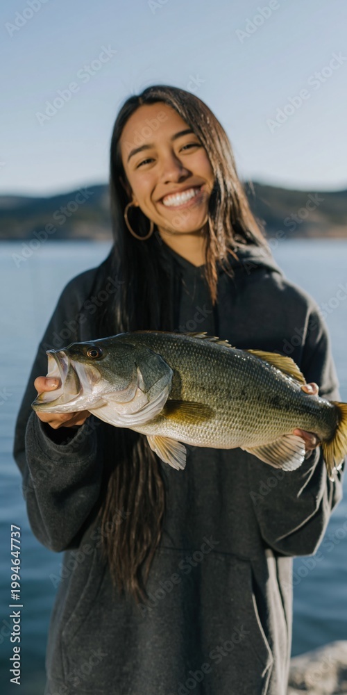 Fototapeta premium Young woman smiling while showing big fish at lake pier