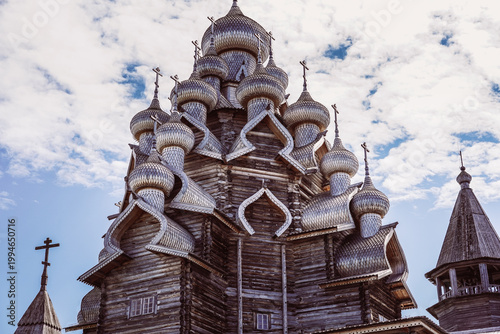 Traditional multi-domed wooden Russian Orthodox church architecture featuring intricate shingle patterns and multiple onion domes against a cloudy sky background.