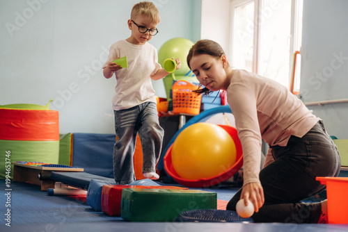 Tableau sur toile Young boy in glasses plays with colorful blocks while woman assists him in a bri