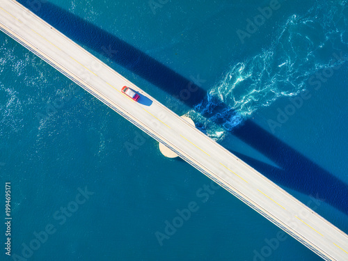 Aerial top down view of a car driving across a bridge over water. Concept of travel, road trip and modern infrastructure. Drone perspective of a highway crossing a river or sea.