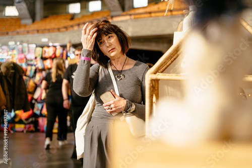 Fotografia Caucasian mature female holding smartphone while browsing handmade market