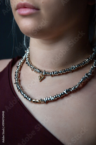 Close-up of woman wearing double-layer metallic choker with heart pendant, burgundy top