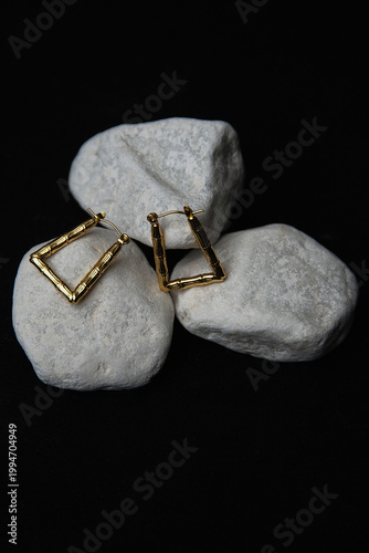Stylish square-shaped gold earrings against white stones, dramatic black backdrop, fashion shot