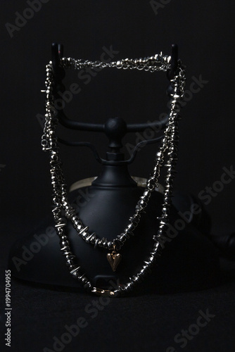 Metallic necklaces rest on black retro telephone, dramatic contrast, fashion accessory display