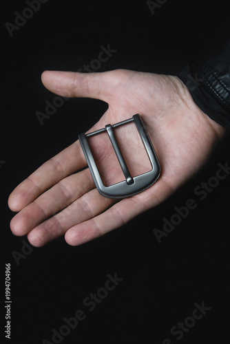 Sleek metallic belt buckle held in hand, dark background, minimalist product shot, modern design