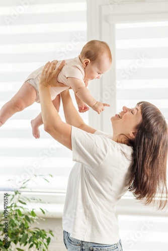 Happy mother lifting baby in the air at home, joyful bonding moment. Mother's Day.