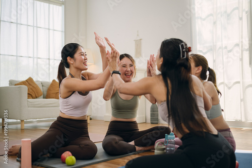 Group of cheerful young Asian women in activewear giving high-fives together in home studio. Joyful friends celebrating after a successful yoga or Pilates workout session. 
