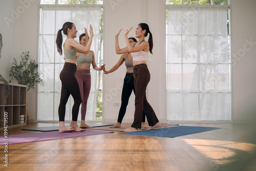 Group of cheerful young Asian women in activewear giving high-fives together in home studio. Joyful friends celebrating after a successful yoga or Pilates workout session.