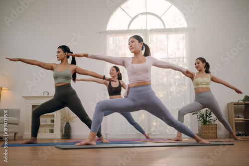 Group of young healthy Asian women practicing yoga class in home studio. Active women performing standing balance and stretch on yoga mats. Concept of flexibility, discipline, and body alignment.