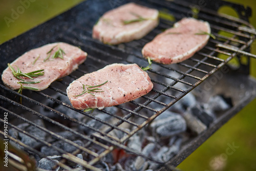 Pork chops grilling on barbecue with charcoal and rosemary