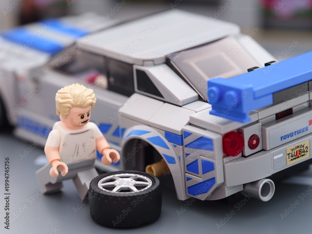 Fototapeta premium Tambov, Russian Federation - August 21, 2025 Lego Brian OConner minifigure changing wheel of his Lego Speed Champions Nissan Skyline GT-R (R34) car.