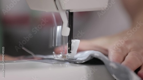 Close-up of a sewing machine needle stitching fabric with a hand guiding the material.