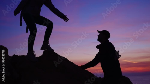 Silhouette of woman help male climber with backpack reach mountain summit, symbolizing teamwork, trust and support, against dramatic twilight sky and inspiring outdoor landscape