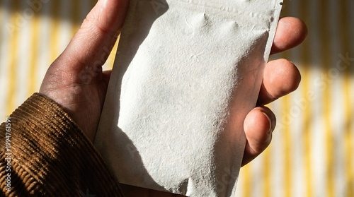 Textured white paper sachet mockup held in hand