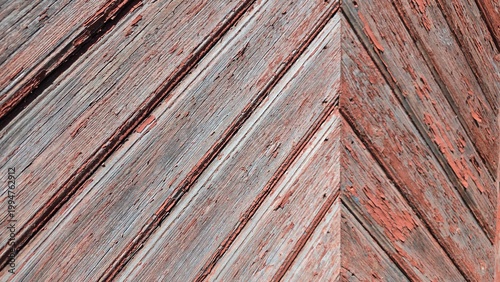 Close-up of weathered wooden planks with pealing terracotta paint arranged in a chevron pattern, showcasing natural wood grain and signs of age, vintage rustic texture concept
