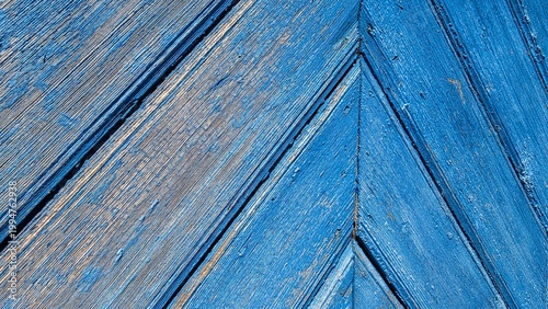 Close-up of aged wooden planks with heavily peeling bright blue paint arranged in a geometric chevron pattern. Vintage rustic texture concept