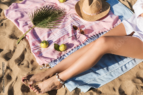 Fotografija Women's legs sunbathing on the beach towel on sand background