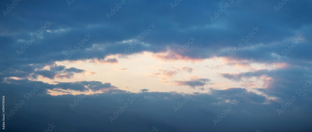 Obraz premium Dramatic twilight sky with a gap between clouds where warm pink-golden hues contrast with deep blue — atmospheric sunset