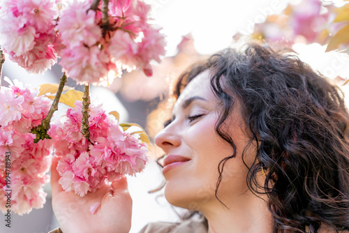 Closeup Portrait of young woman near blooming pink sakura. Spring. Unity with nature.
