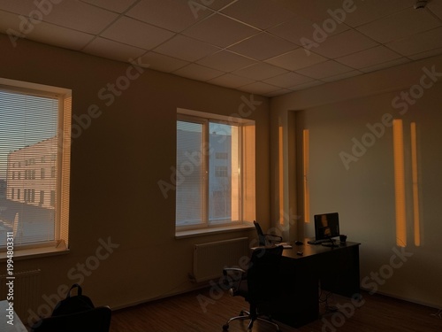 Sunlight streams through windows casting shadows in a quiet modern office with empty desks and chairs.