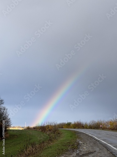 A vibrant rainbow arches over a serene landscape, illuminating a tranquil rural scene after rainfall.