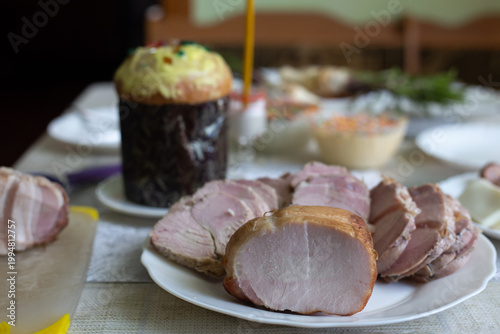 Sliced ​​ham on a plate. Easter cake and various dishes behind.