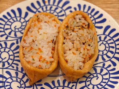 High angle close-up of two inarizushi on patterned ceramic plate