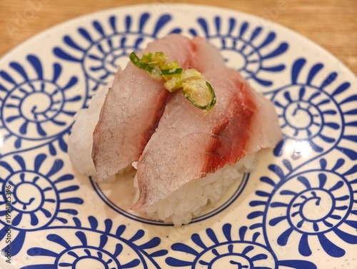 High angle view of two fresh raw fish nigiri sushi topped with green onion and ginger, served on patterned ceramic plate