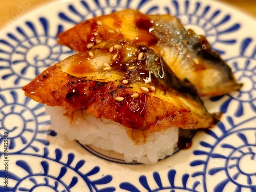 High angle view of unagi nigiri sushi with dark glaze and sesame seeds, served on a patterned ceramic plate