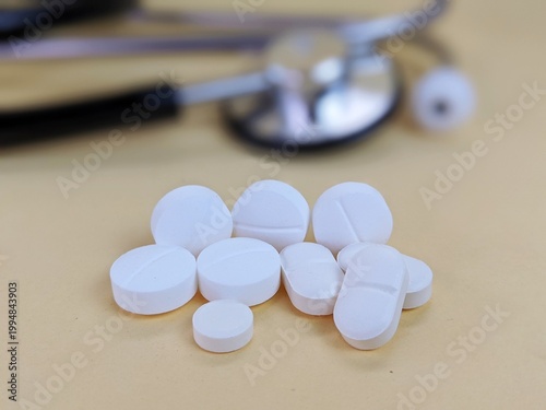 White tablets with blurry stethoscope on light surface symbolizing medicine, healthcare and pharmaceutical treatment in clinical practice.