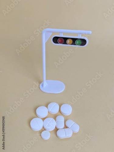 White traffic light model with red, yellow, green signals beside assorted tablets symbolizing healthcare caution and medication control. Healthcare concept