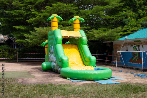 Inflatable tropical-themed water slide with palm tree decorations set outdoors in a green park area, colorful summer playground attraction for children.