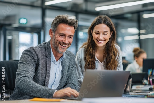 Two colleagues happily work together at a laptop in a modern office