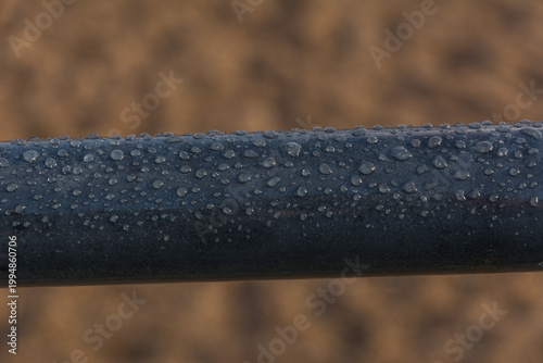 Close-up of Water Droplets and Morning Dew on a Dark Pipe in Agriculture
