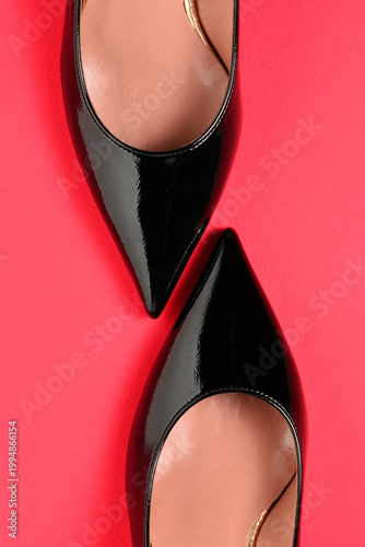 Black patent leather stiletto heels on red surface, vertical composition.