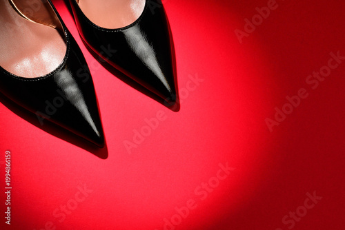 Black patent leather high heels on red background with central light spot.