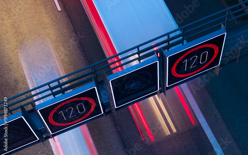 Electronic road signs displaying speed limits over highway traffic at night,