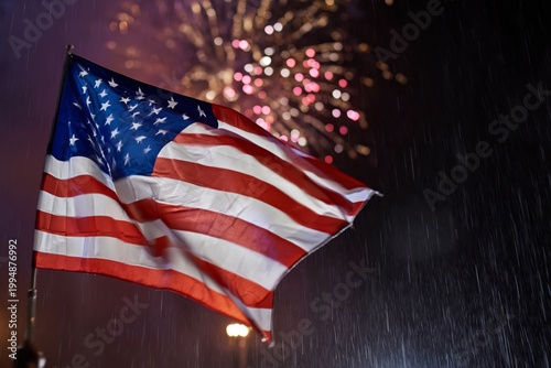 Fireworks Light up the Sky Behind a Waving American Flag in the Rain During a...