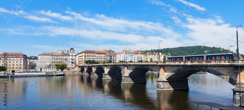 Photos Tram crossing a bridge over a river in Prague with city buildings in the background