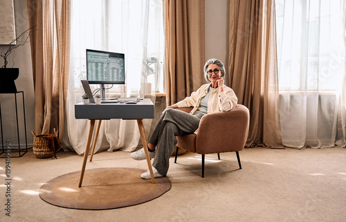 Tableau sur toile Mature woman relaxing in a comfortable armchair in a cozy beige-toned living roo