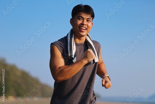 Billede på lærred Young Asian man jogging on the beach in the morning light.
