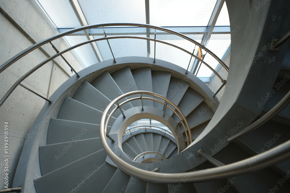 Obraz premium Curving concrete spiral staircase with metal railing indoors