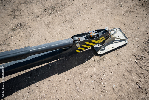 Hydraulic stabilizer outrigger with steel foot plate on dirt ground, industrial machine support detail for construction safety, lifting and site setup